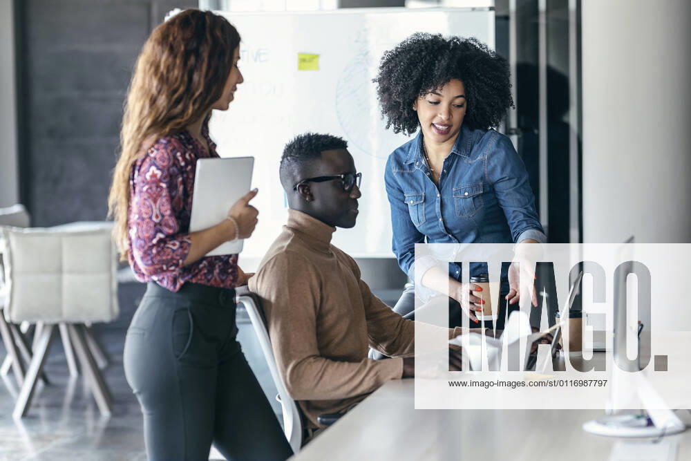 Female entrepreneur gesturing while discussing over laptop with colleagues at office model released Symbolfoto property released JSRF01495
