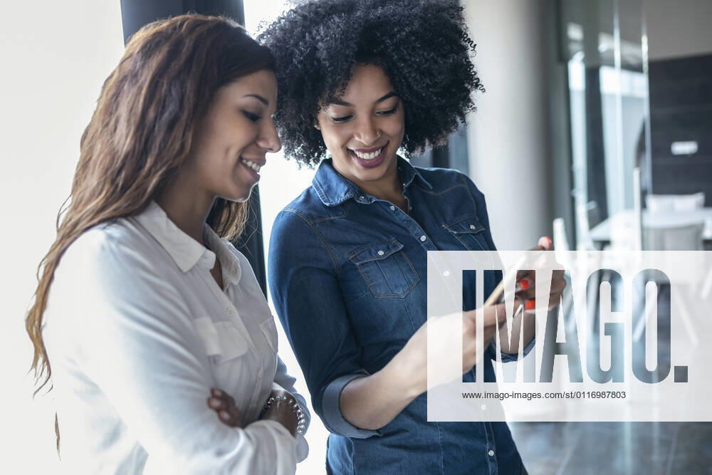 Smiling female entrepreneurs discussing over mobile phone at office model released Symbolfoto property released JSRF01501