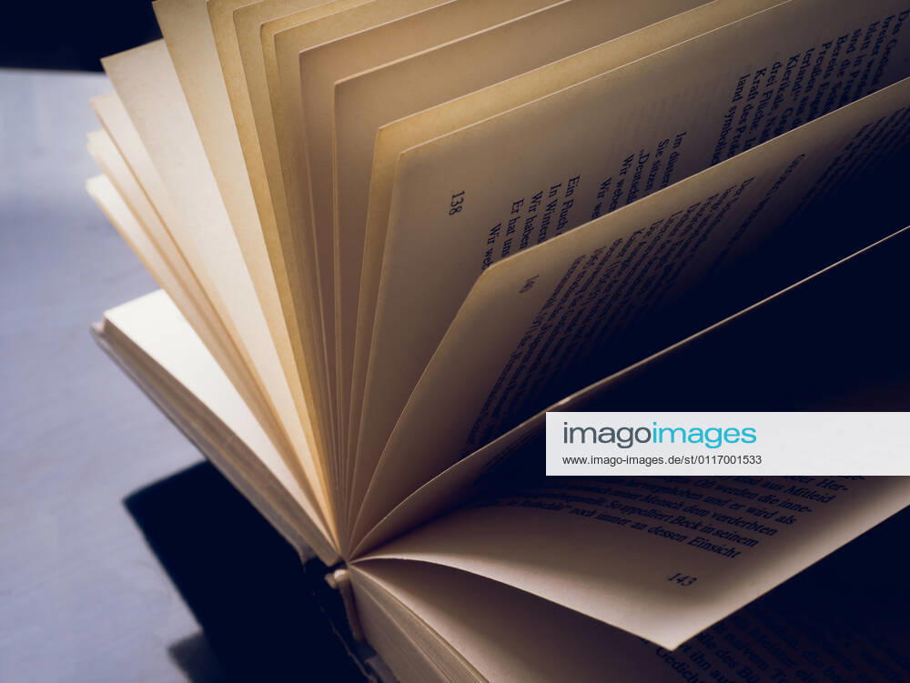 Opened and fanned book in front of dark background with text free space 1028901446