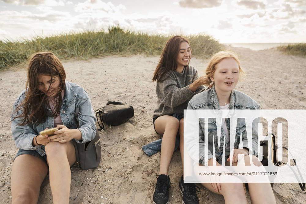 IMAGO Creative, Jahreszeit Sommer, Sommerferien IMAGO Creative: Landleben - Alfresco, Draußen Teenage girl using smart phone while female friends sitting on sand at beach Sweden, Malmo, model released
