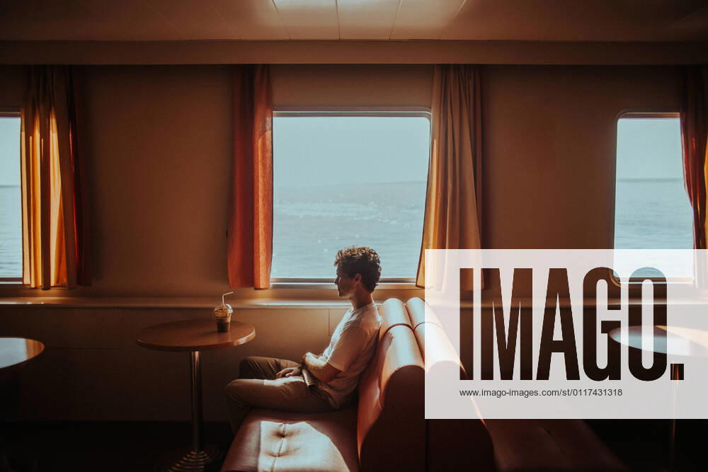 Side view thoughtful young male wearing casual summer clothes sitting on soft couch while travelling in ferry on rippling sea in Greece bright, Model released