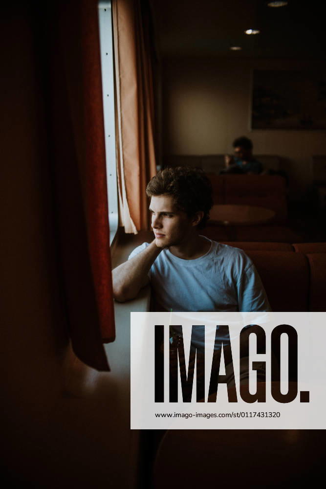 Side view thoughtful young male wearing casual summer clothes sitting on soft couch while travelling in ferry on rippling sea in Greece bright, Model released