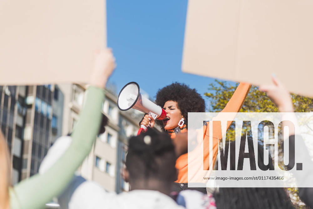 IMAGO Creative: Resilienz IMAGO Creative: Frauenmonat, Feministischer Aktivismus IMAGO Creative: 2022 Aussichten African American female social justice warrior with speaker against crop anonymous multiracial people with placards fighting for human rights in town, Model released