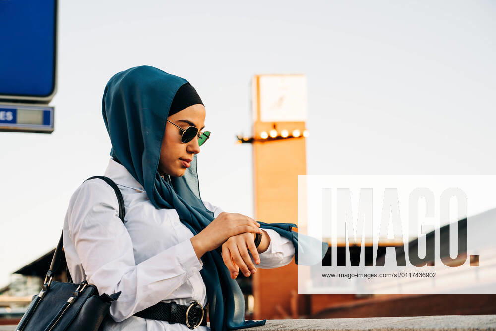 IMAGO Creative: Ruhe im Chaos IMAGO Creative: 2021 Favoriten Side view of Muslim female in hijab standing on platform at railway station and checking time on wristwatch while waiting for train