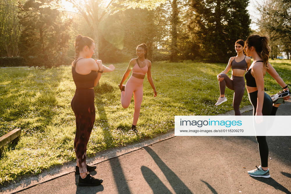 IMAGO Creative: Sommer, Sommertage im Stadtpark Young multiracial female athletes in sportswear stretching arm and legs on asphalt footpath in town on sunny day, Model released