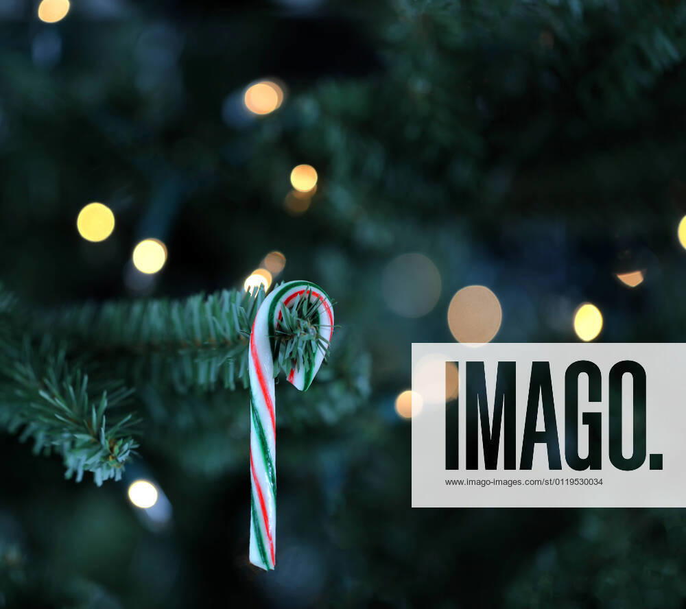 Traditional artificial Christmas tree with candy cane and white lights glowing in background