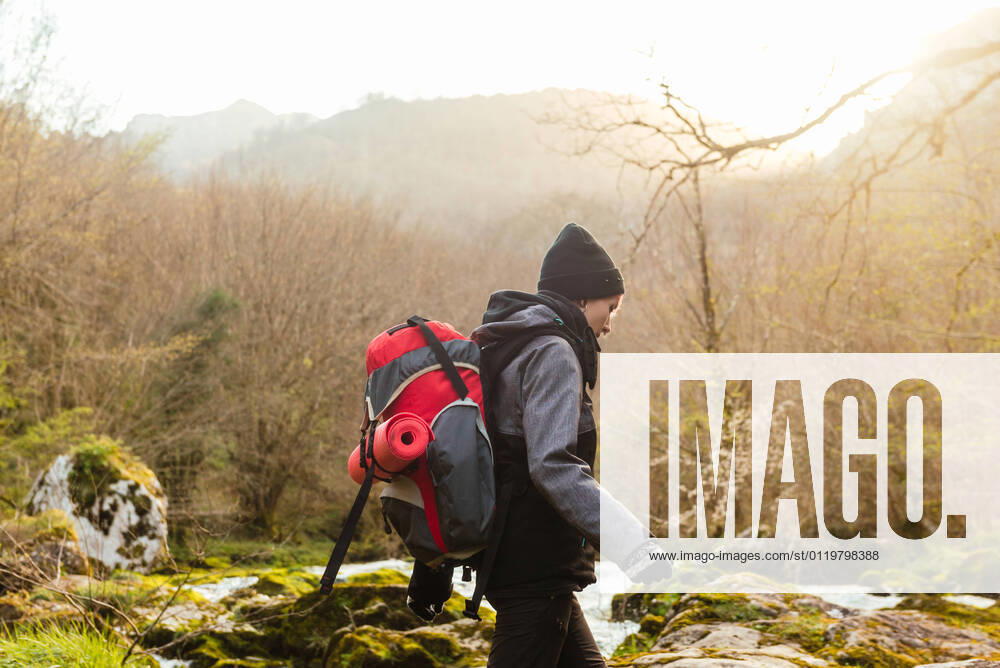 IMAGO Creative: Digitale Welt, Verzicht auf Technologie Side view of explorer with backpack walking on mossy rocks near rapid stream of water flowing among forest with leafless trees, Model released