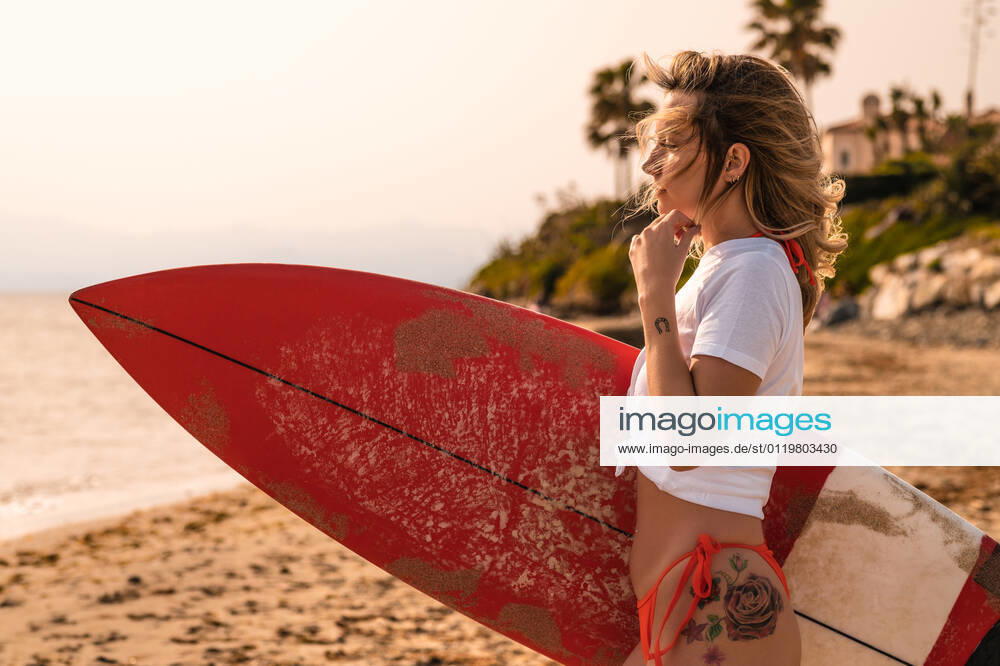 Female surfer with surfboard looking away on sandy coast against palm tree in daytime, Model released, Property released