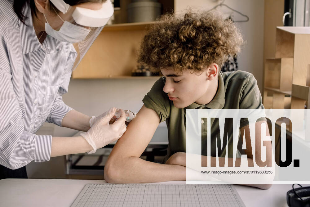 IMAGO Creative: 2022 Aussichten IMAGO Creative: NGO, Rehabilitation und Gesundheitswesen Boy with curly brown hair looking at nurse injecting medicine at home Sweden, Stockholm, model released, property released