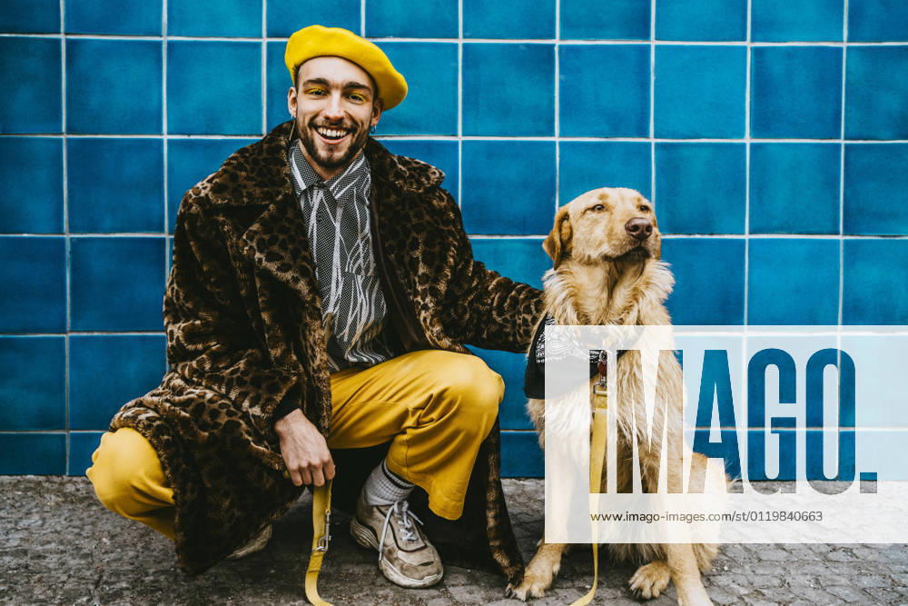 Full length of smiling man crouching by dog against blue tiled wall Berlin, Germany, model released
