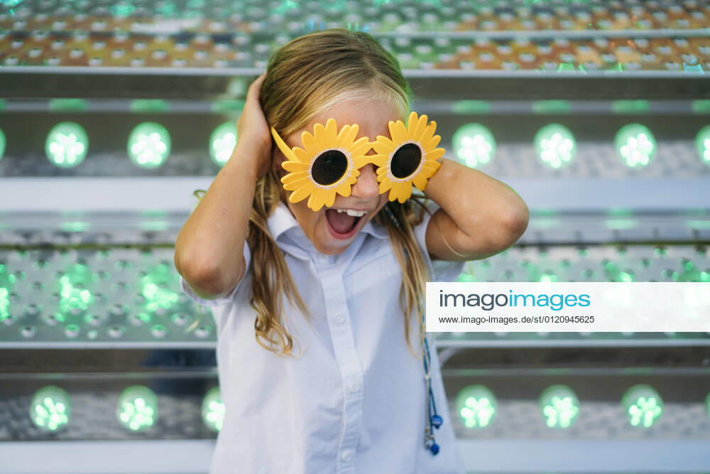 Cute girl sitting on metallic stairs. She is wearing funny flower-shaped sunglasses in the amusement park, Model released