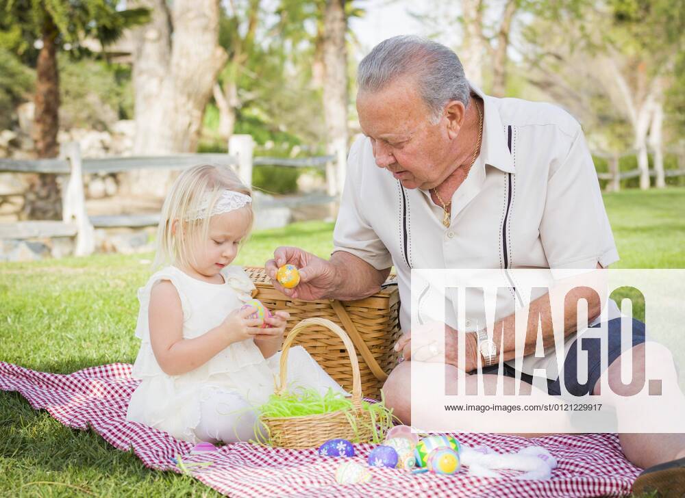 Lovely grandfather and granddaughter enjoy easter eggs on a picnic blanket in the park