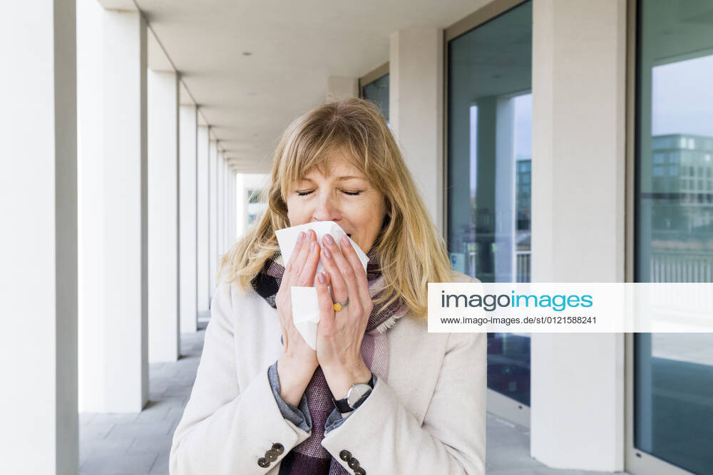 Mature woman sneezing while standing at corridor model released Symbolfoto IHF00447