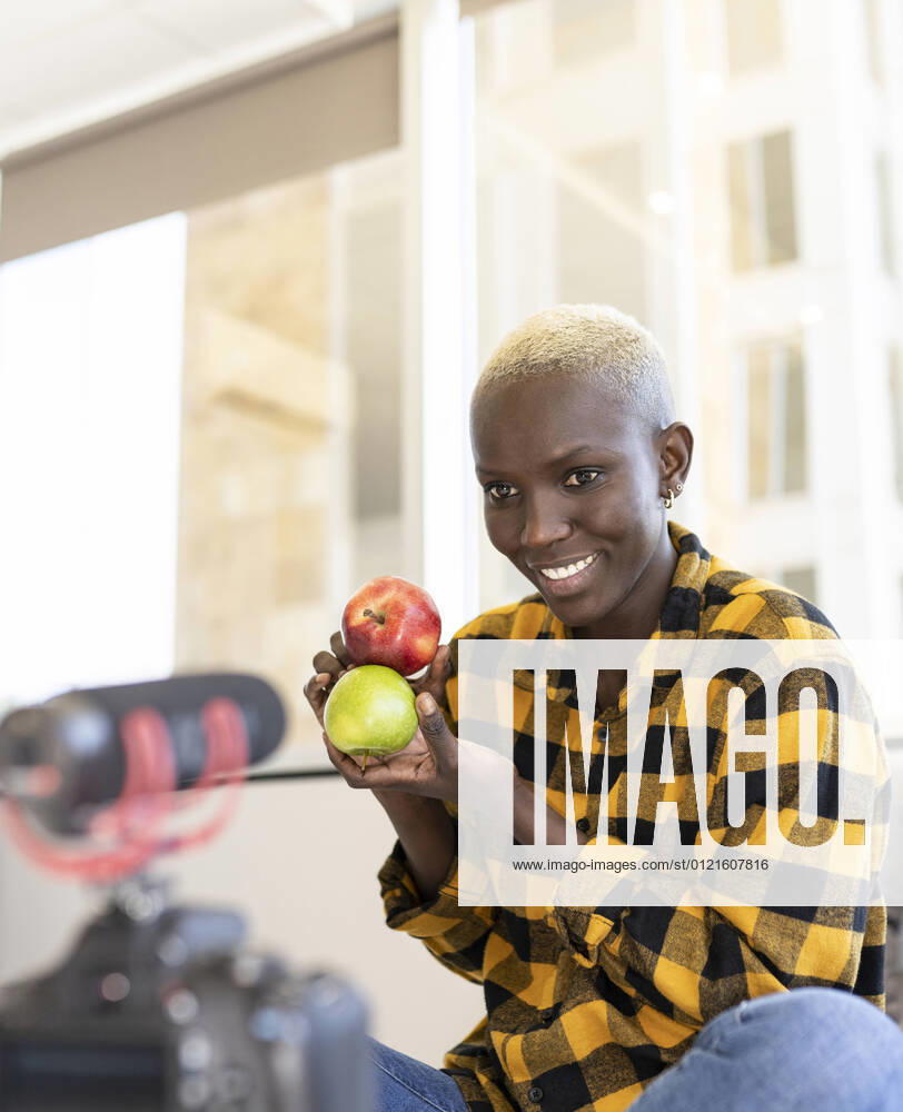 Short haired woman holding apple while vlogging at home model released Symbolfoto property released JCCMF02323