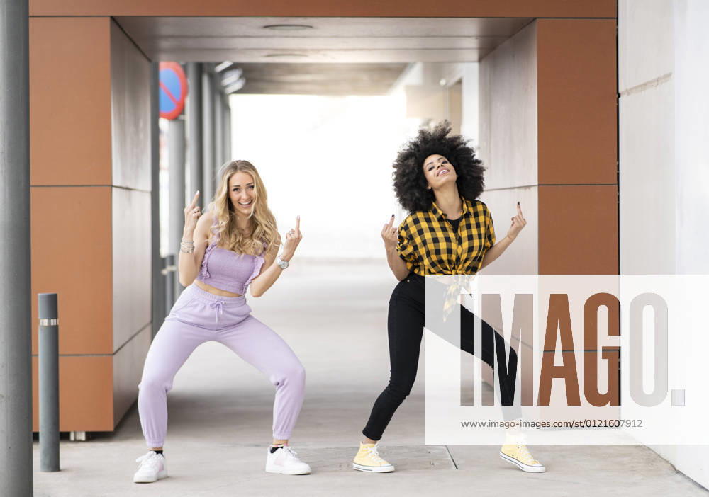 Female friends making obscence gesture while dancing at parking lot model released Symbolfoto JCCMF02353