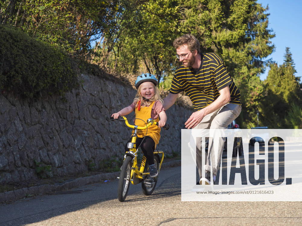 IMAGO Creative: Vaterschaft Father supporting daughter while cycling on road model released Symbolfoto LAF02713