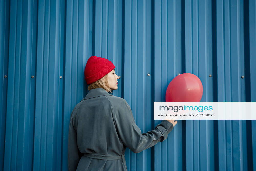 Mid adult woman holding red balloon by blue shutter model released Symbolfoto RCPF00986