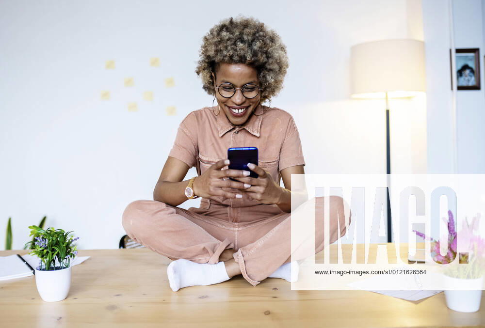 Female professional using smart phone while sitting cross-legged on desk at home office model released Symbolfoto property released RFTF00067