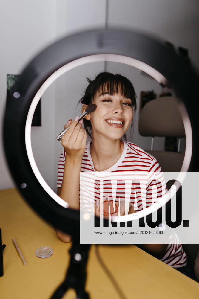 Smiling female influencer applying make-up while vlogging at studio model released Symbolfoto property released TCEF01763