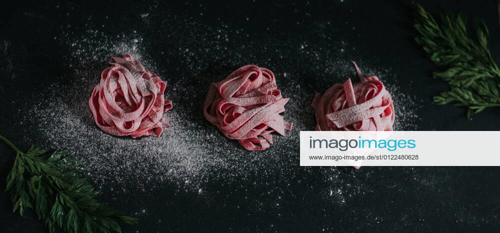 Appetizing vegan beetroot pasta of pink color served on black table in studio