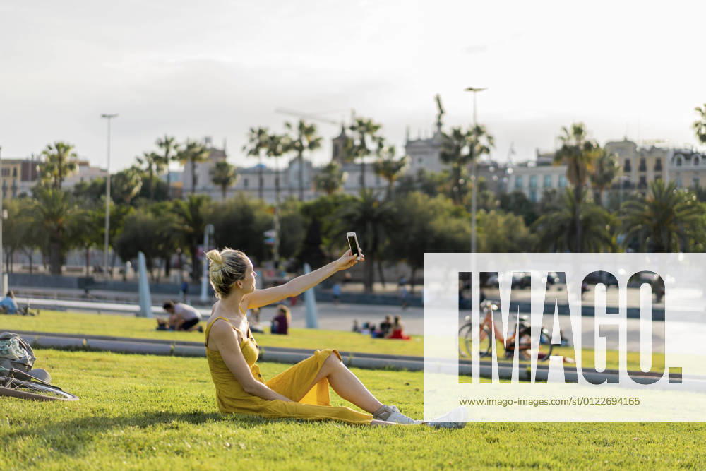 IMAGO Creative: Sommer, Sommertage im Stadtpark Young woman taking selfie through smart phone while sitting at park model released Symbolfoto AFVF08865