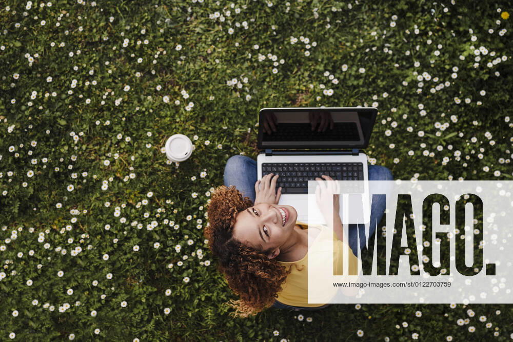 IMAGO Creative: Jahreszeit Frühling, Frühlingsanfang am 20. März IMAGO Creative: Klimawandel - Zukunft und Innovation Young woman looking up while sitting with laptop on meadow amidst flowers model released Symbolfoto EBBF03699