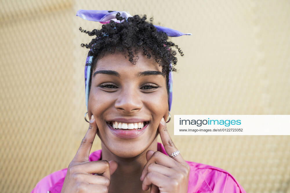 Smiling young woman touching cheeks with index fingers model released Symbolfoto JCCMF02523