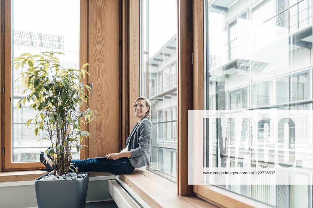 Female entrepreneur smiling while sitting by window model released Symbolfoto property released JOSEF04784