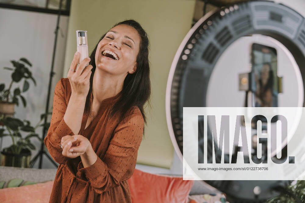 Laughing female influencer holding foundation while vlogging at home model released Symbolfoto property released MFF08081