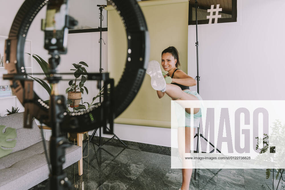 Female fitness trainer showing kicks near backdrop while vlogging at home model released Symbolfoto property released MFF08095