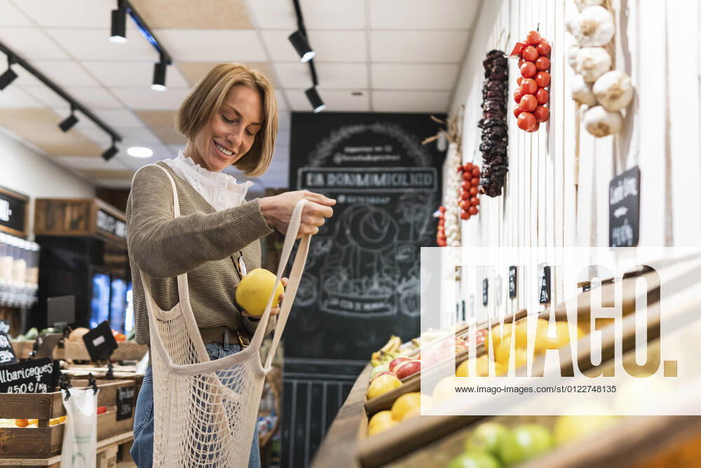 IMAGO Creative: Klimawandel - Zukunft und Innovation Woman collecting fruit in mesh bag while shopping in supermarket model released Symbolfoto property released PNAF01915