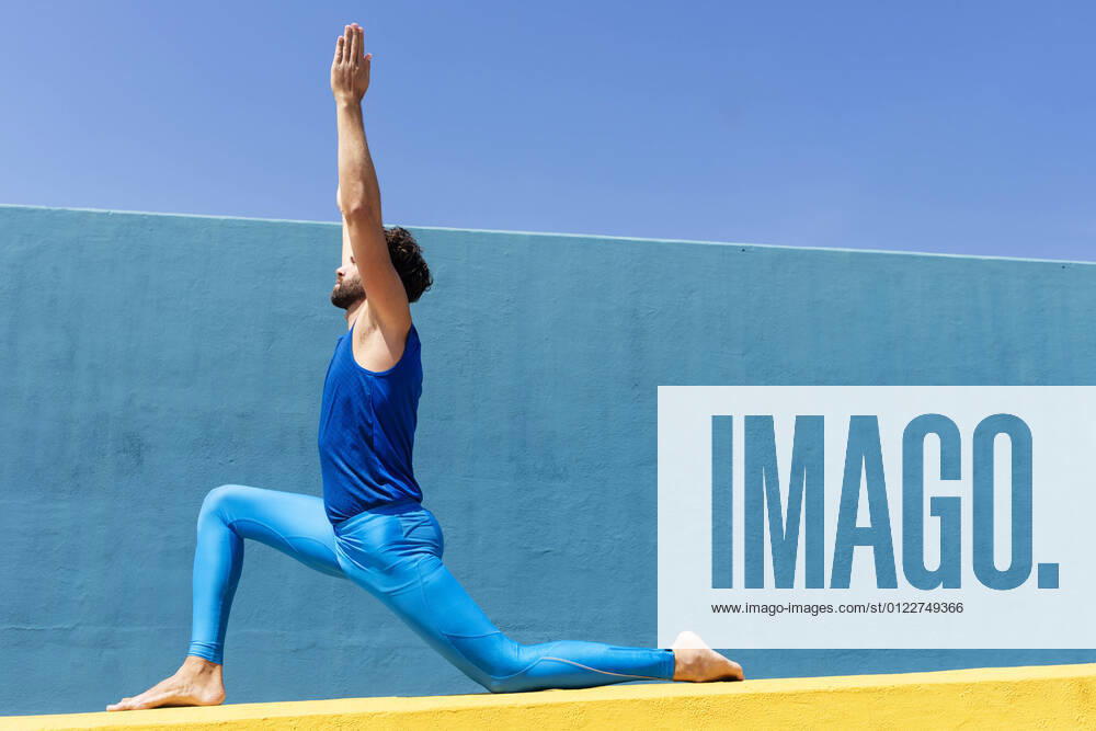 Mid adult man with hands clasped practicing yoga on retaining wall during sunny day model released Symbolfoto RFTF00096