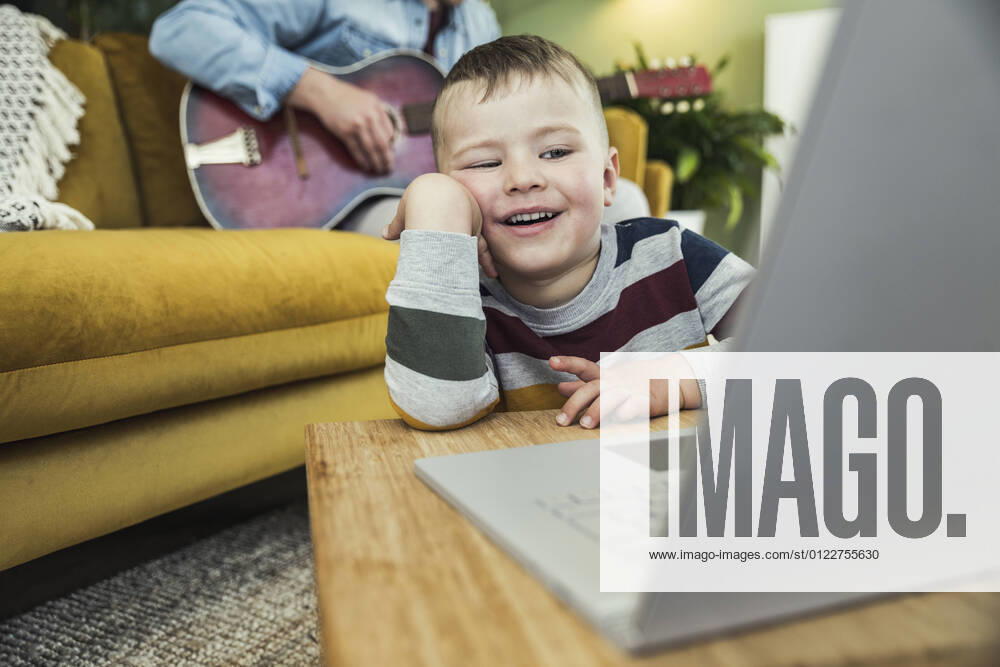 Cute boy watching video on laptop while father playing guitar in living room model released Symbolfoto property released UUF23410