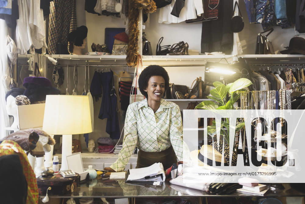 IMAGO Creative: Retro-Revival Smiling female owner looking away while standing at counter in clothing store Sweden, Stockholm, model released, property released