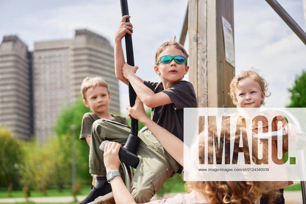 Company of cute kids playing together on playground in city while having fun on sunny day in summer, Model released