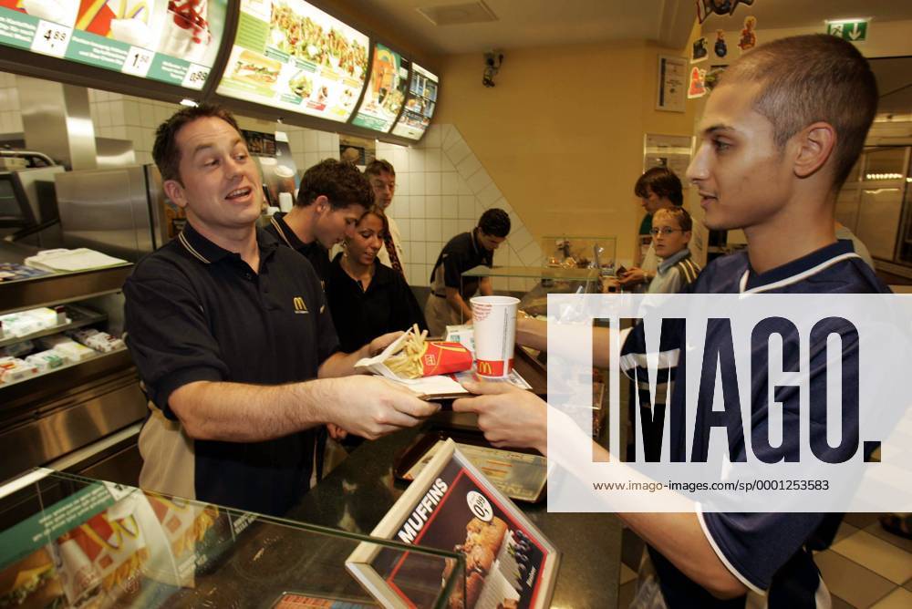 Einen Tag lang Verkäufer bei McDonalds: Wayne Hynes (li.) überreicht einem Kunden entsprechend der Firmenphilosophie gutgelaunt ein Hamburger Royal TS Menu, hi. läßt sich Goalie Leonhard Wild (beide Hamburg) die Kasse erklären Eishockey DEL Herren Hamburg Freezers 2004, Shooting, Fotoshooting, Fototermin, MacDonalds, Mc Donalds, Mac, Fast Food Gruppe Hamburg