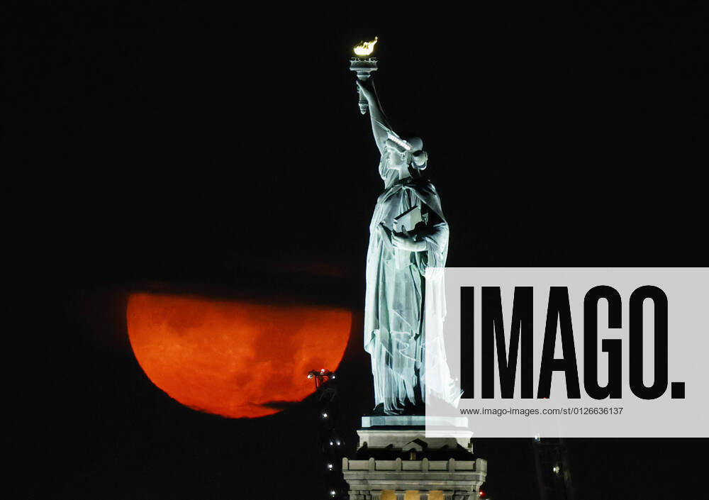 A full Buck Moon, partially obstructed by clouds, sets behind the Statue of Liberty in New York City on Friday, July 23, 2021. NYP20210723101 JohnxAngelillo