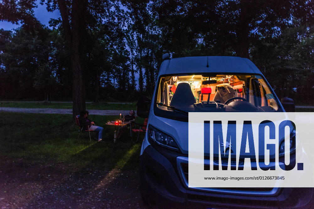 Campers sitting on camping chairs in front of their camper at blue hour on a warm summer evening Baden Württemberg, Germany On the road with a campervan