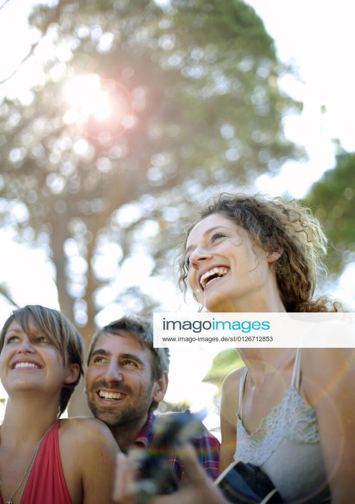Smiling woman playing guitar with friends at park model released Symbolfoto AJOF01534
