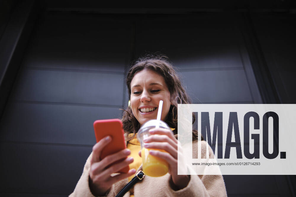 Smiling young woman with smoothie using smart phone near black door model released Symbolfoto ASGF00635