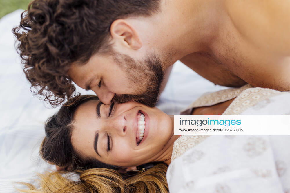 Affectionate man kissing happy girlfriend with eyes closed lying on blanket model released Symbolfoto EGHF00093