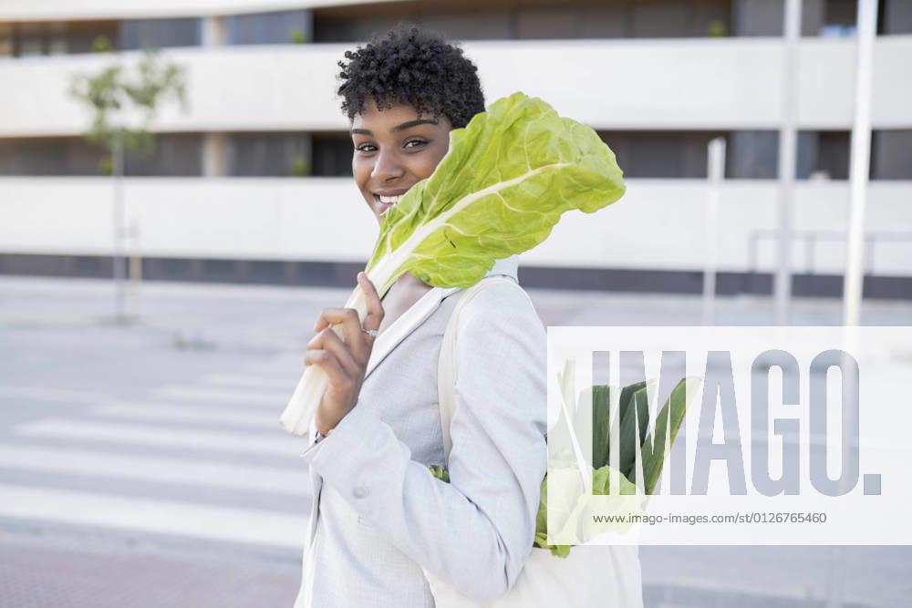 IMAGO Creative: Veganuary, fleischlos leben Smiling businesswoman holding leaf vegetable in city model released Symbolfoto JCCMF02921