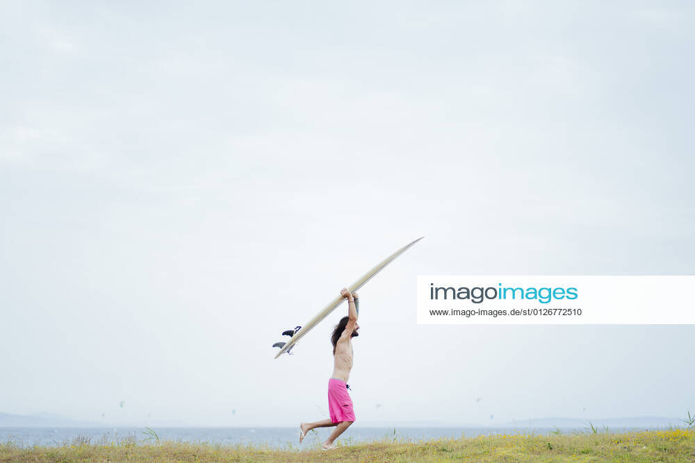 Carefree shirtless man carrying surfboard while running on meadow model released Symbolfoto property released PGF00620