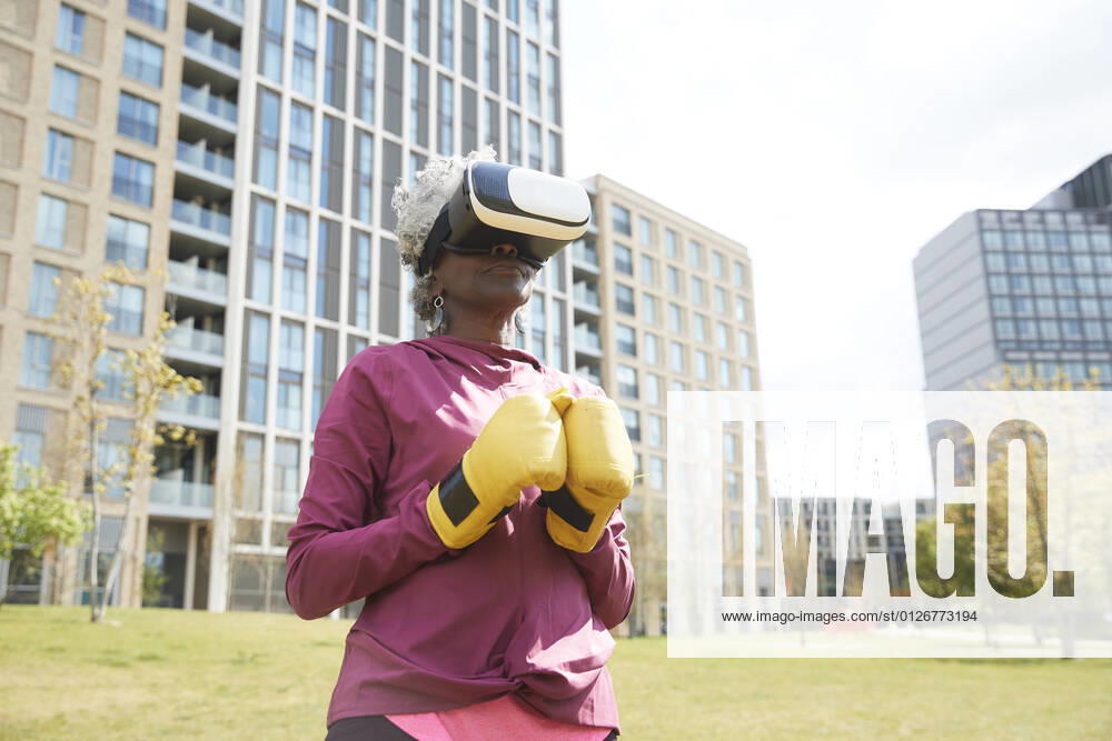 Senior woman with boxing gloves wearing virtual reality headset in park model released Symbolfoto PMF01992