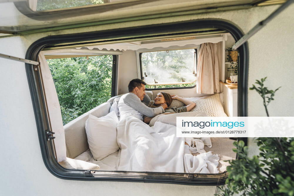 Loving man embracing girlfriend while lying on bed seen through camper window model released Symbolfoto property released VPIF04370