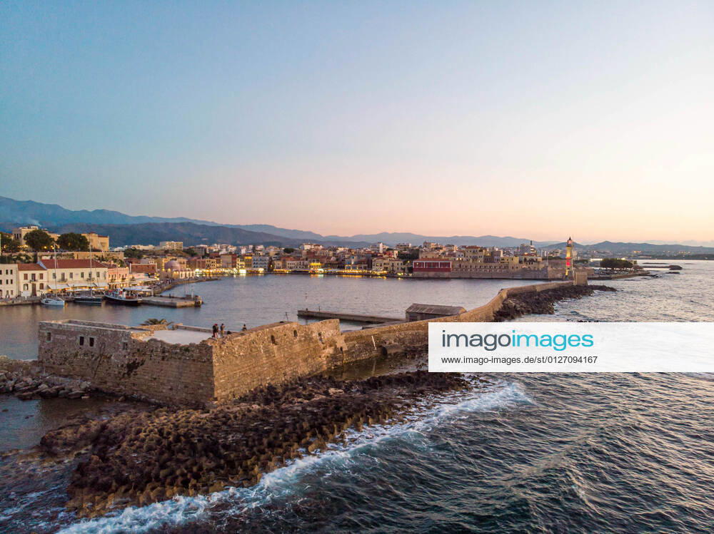 Aerial View Of Chania Town In Crete Island Panoramic aerial view of a drone during the magic hour after the sunset of the beautiful old Venetian harbor of Chania town with the lights illuminating of the amazing lighthouse, mosque, venetian shipyards and old the monuments and landmarks near the port and the sea. Greece is trying to boost its tourism and give privileges to vaccinated against Covid-19 Coronavirus pandemic, international tourists and locals, as the country is heavily depended from the travel and tourism industry despite the concerning raising number of cases with the Covid-19 Coronavirus Delta mutation variant. Chania, Crete Island, Greece on June 27, 2021 Chania Greece economou-notitle210727_npBIt