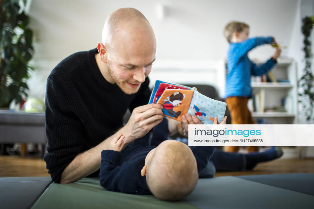 Symbolic photo A father plays with his baby while a second child plays for himself in the background Berlin, 02 02 2021 Berlin Germany