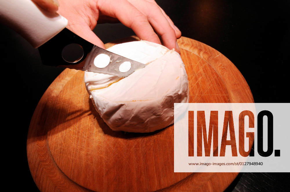 Cutting a camembert in the middle with a cheese knife on a round wooden board camembert, a creamy soft cheese