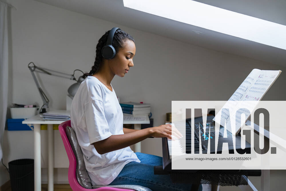 IMAGO Creative: Bildung, Musikerziehung Teenage girl playing piano while sitting at home model released Symbolfoto property released MGIF01029