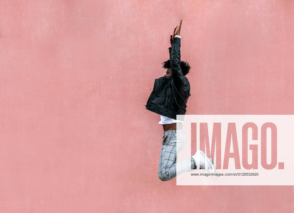 Mid adult man with arms raised jumping by pink wall in city model released Symbolfoto MGOF04458